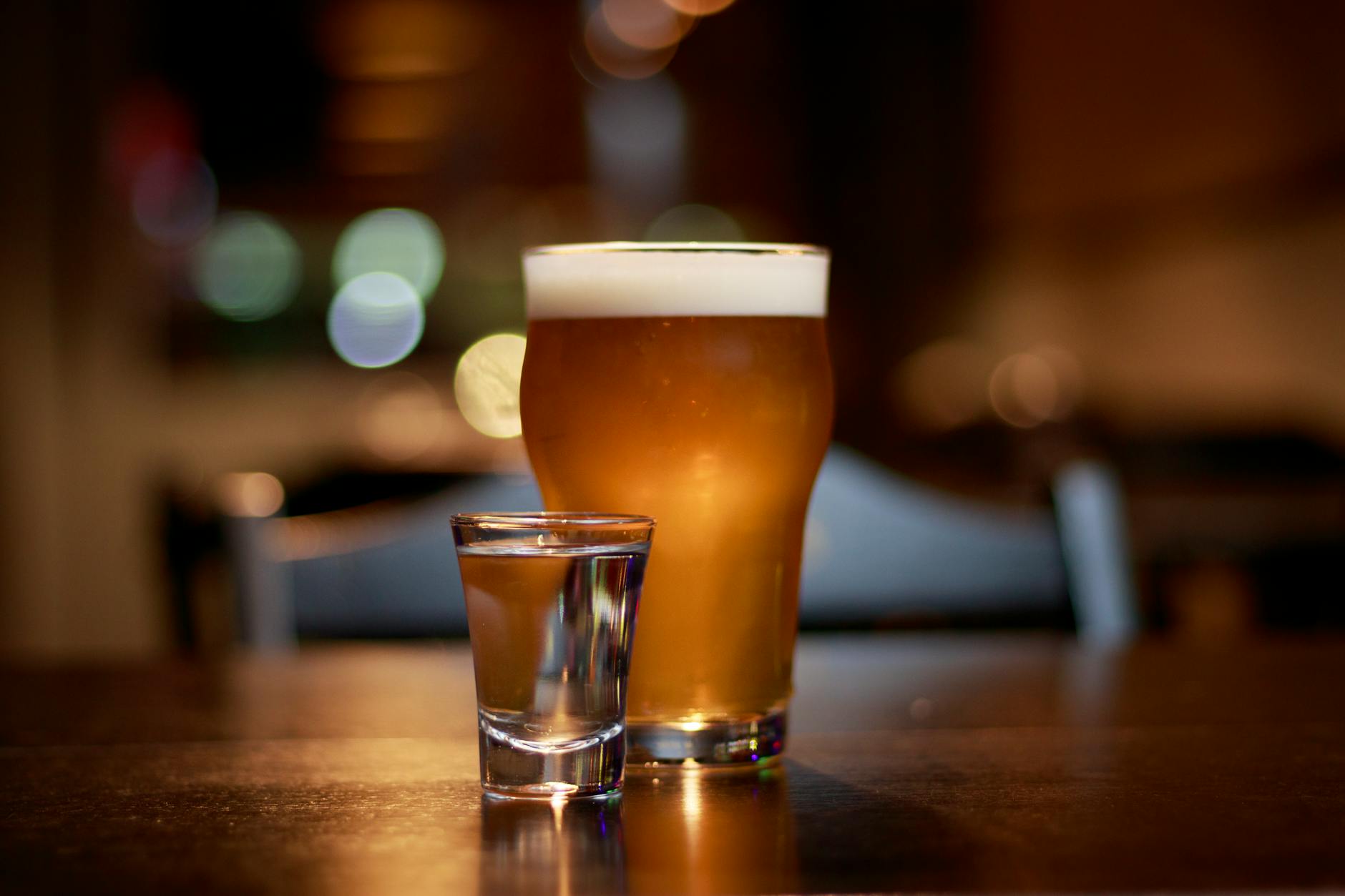 A glass of beer and a shot glass on a table