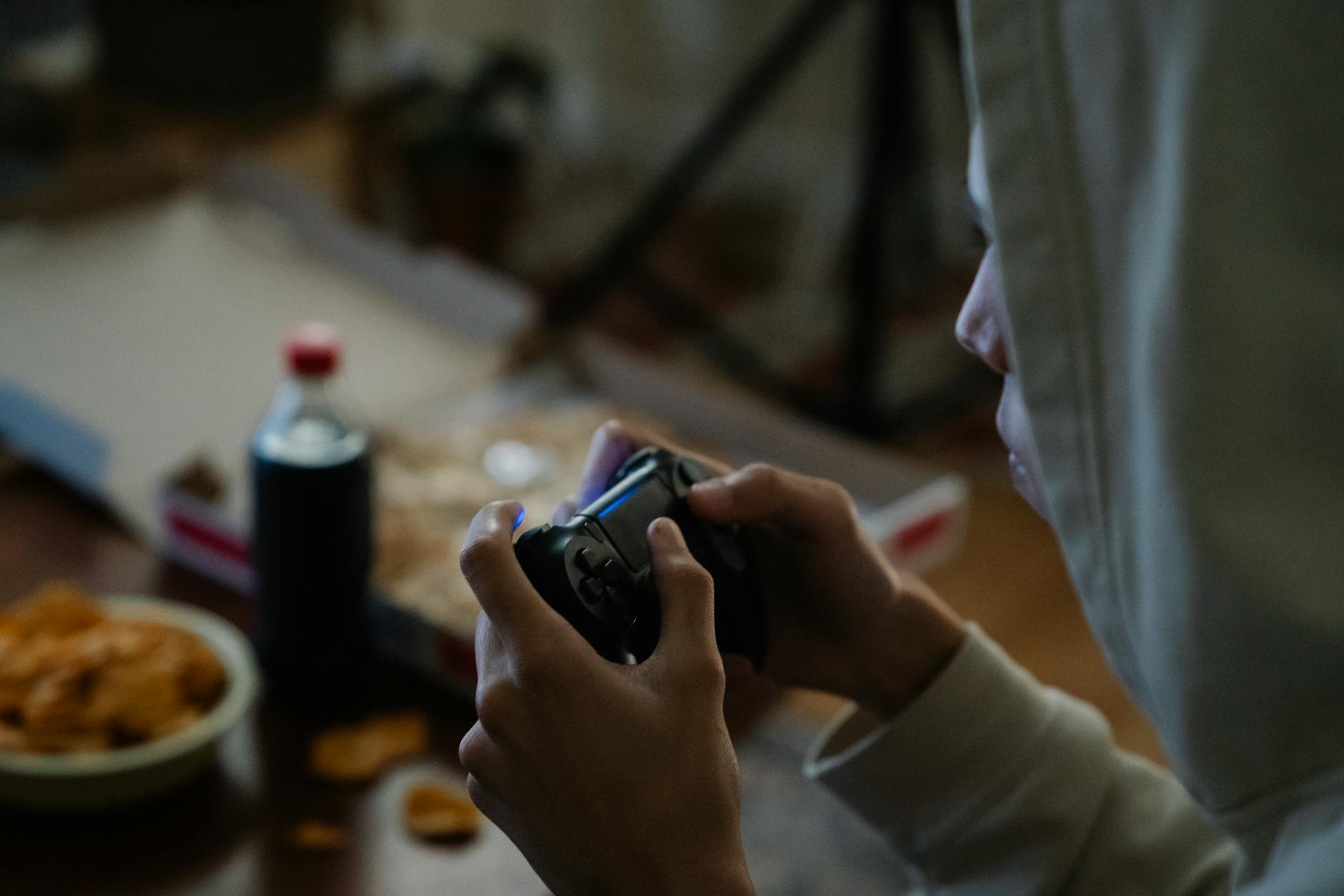 Crop gamer with console controller playing video game in house