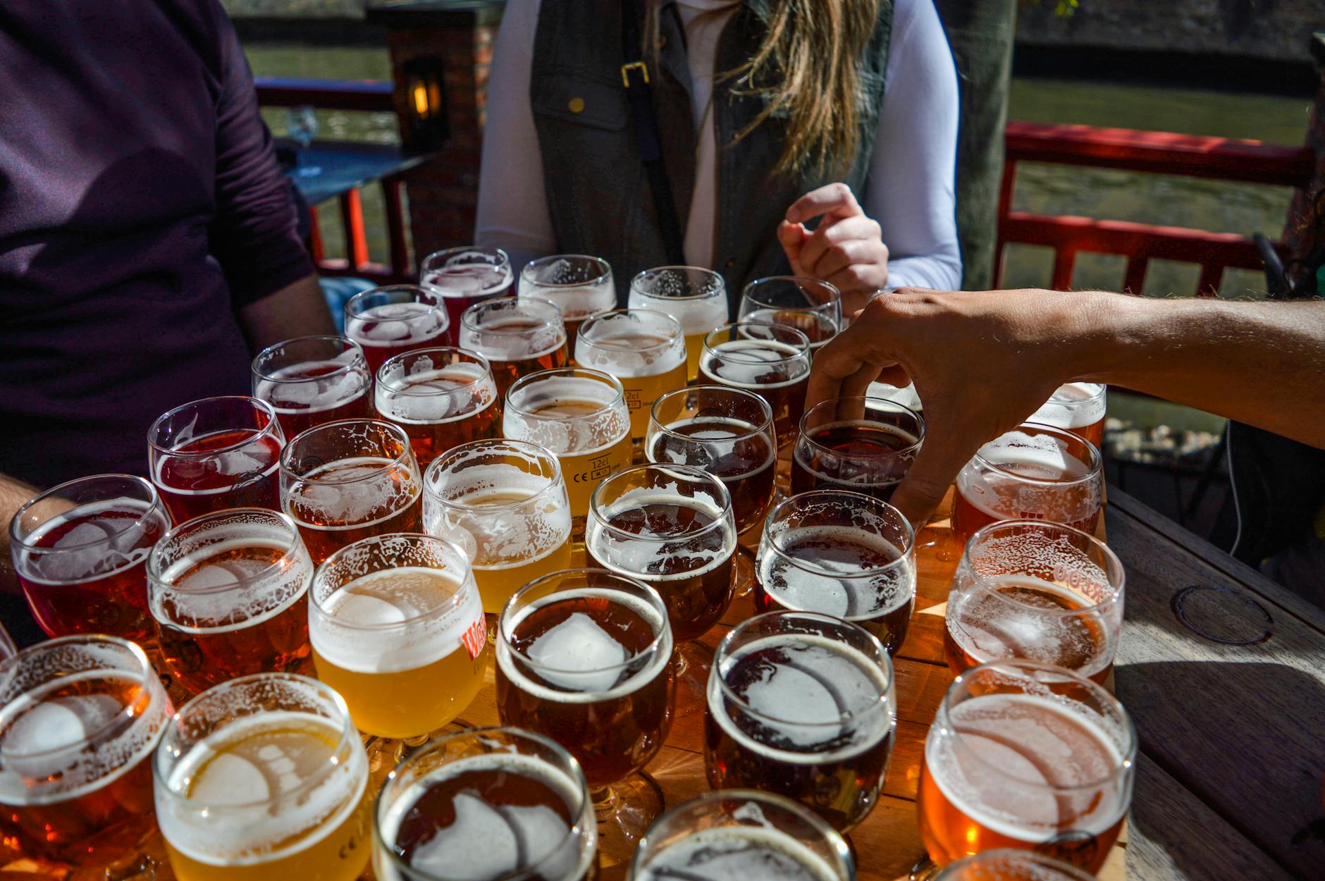 High angle of crop faceless friends tasting various types of craft beer while relaxing together in street cafe on sunny day