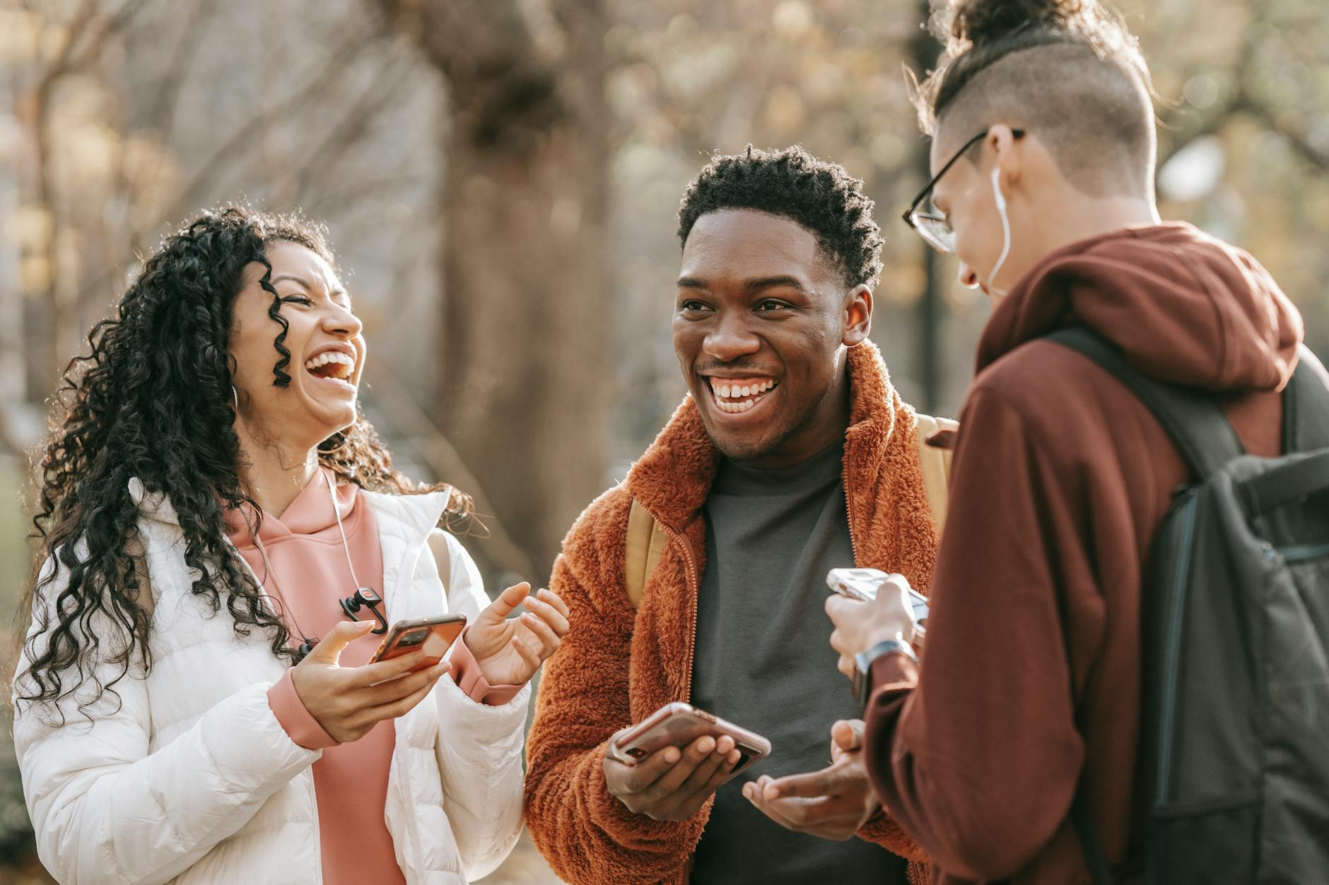 Laughing diverse friends with smartphones in park