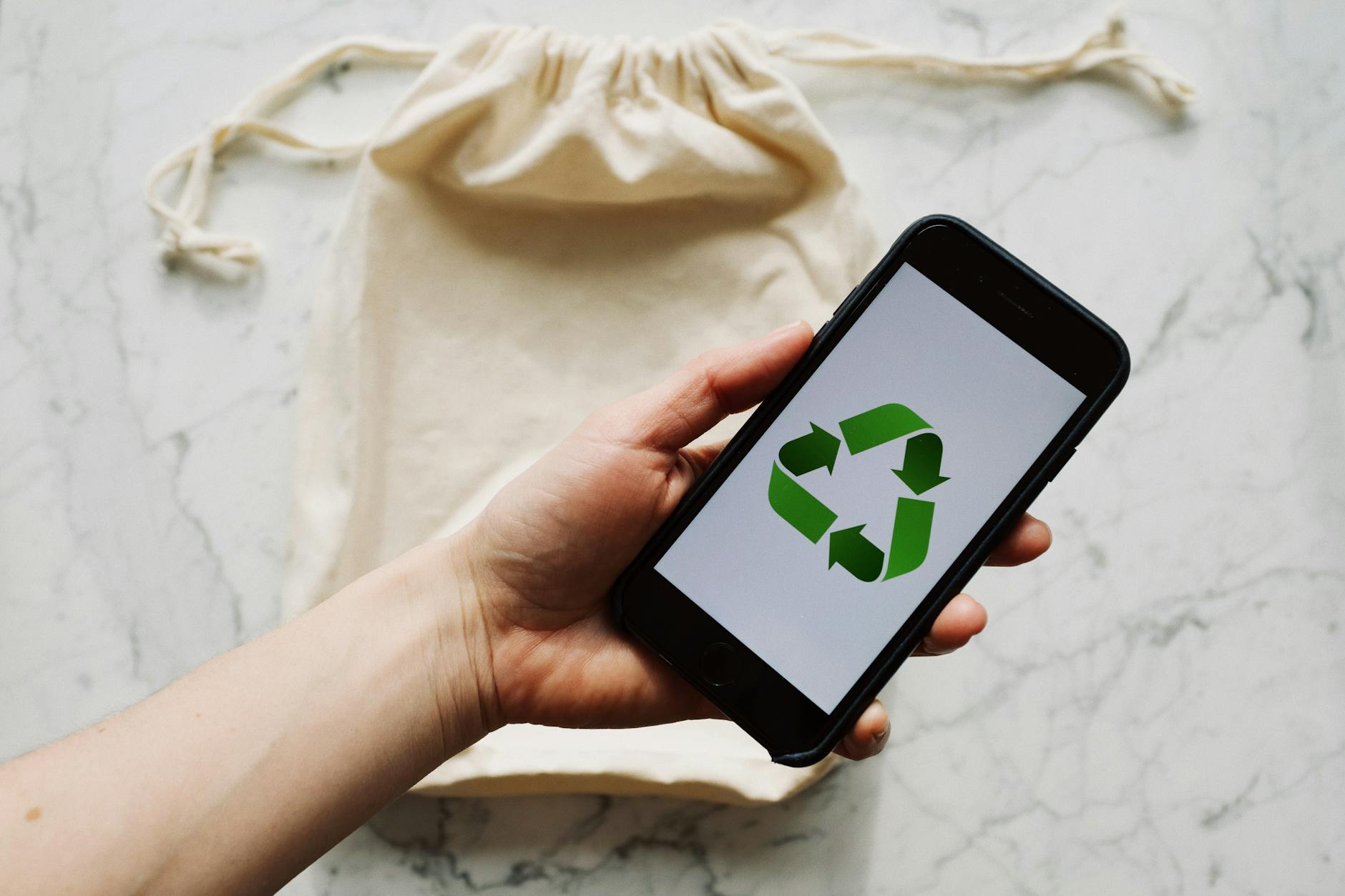 Anonymous crop person holding smartphone over white textile bag on marble table