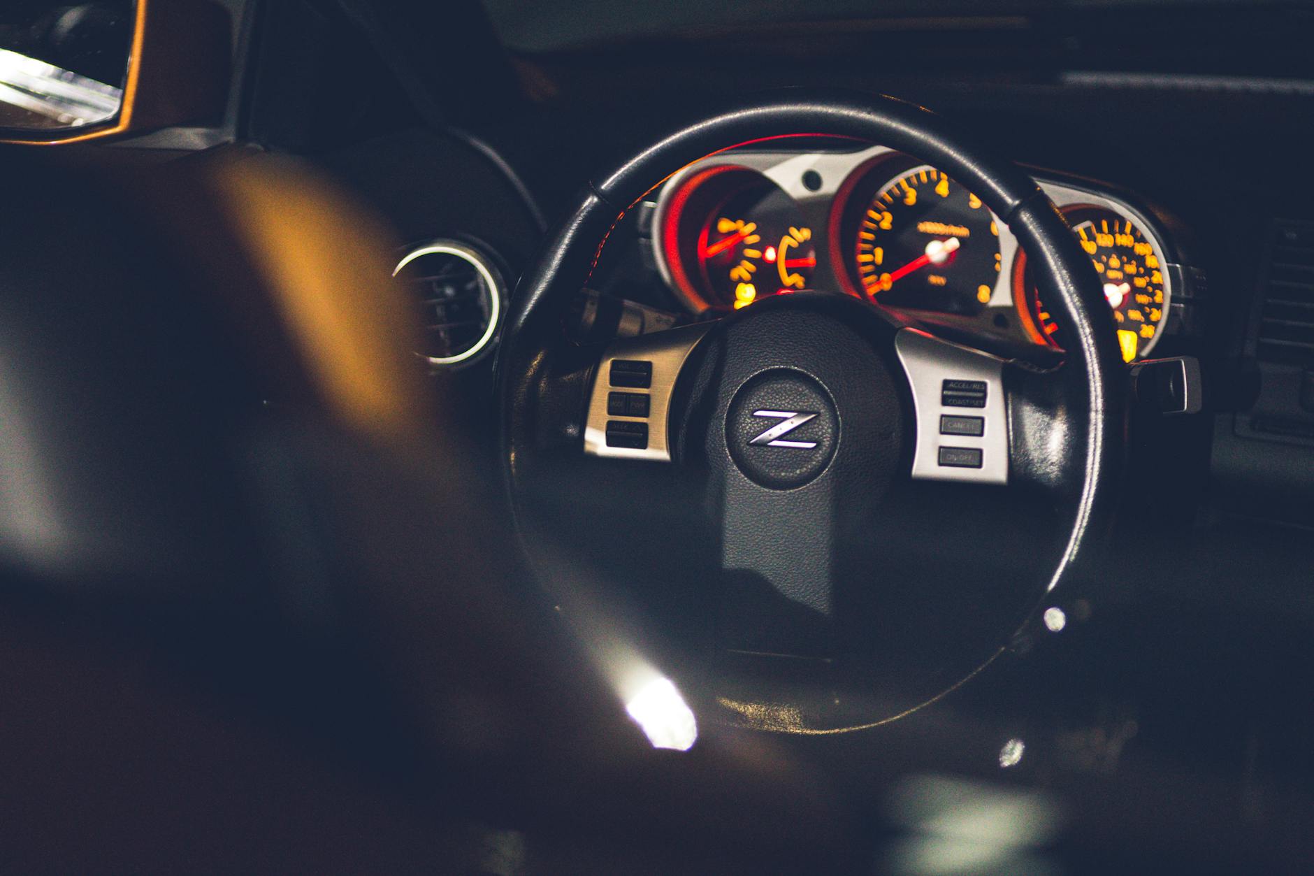 Contemporary auto interior with shiny steering wheel and bright instrument panel near leather seat in evening