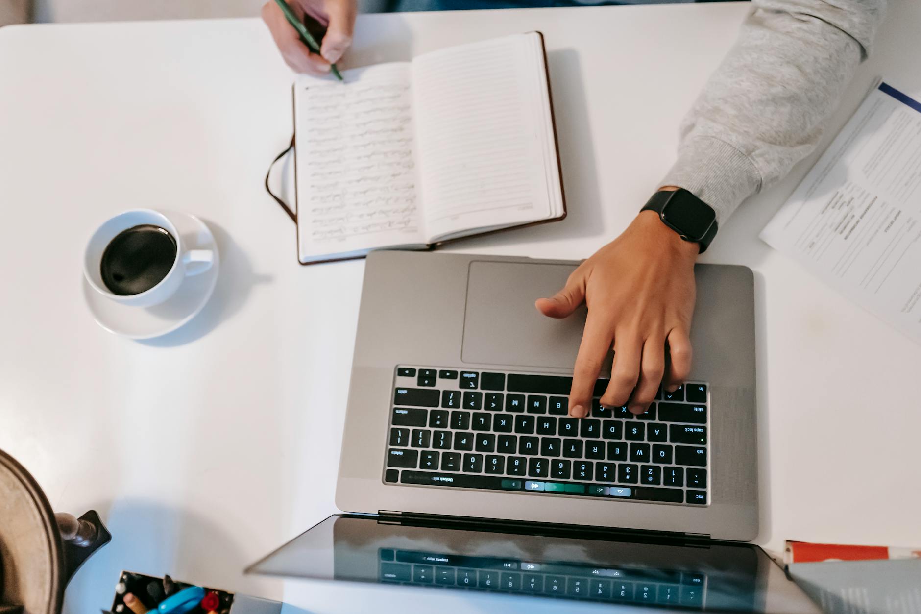 Faceless freelancer typing on laptop and writing in journal indoors