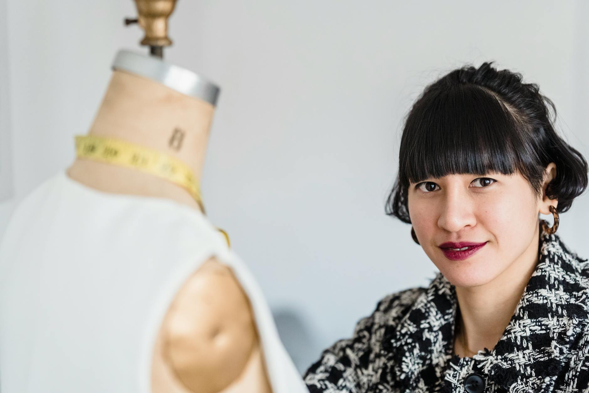 Smiling Asian tailor against mannequin in studio