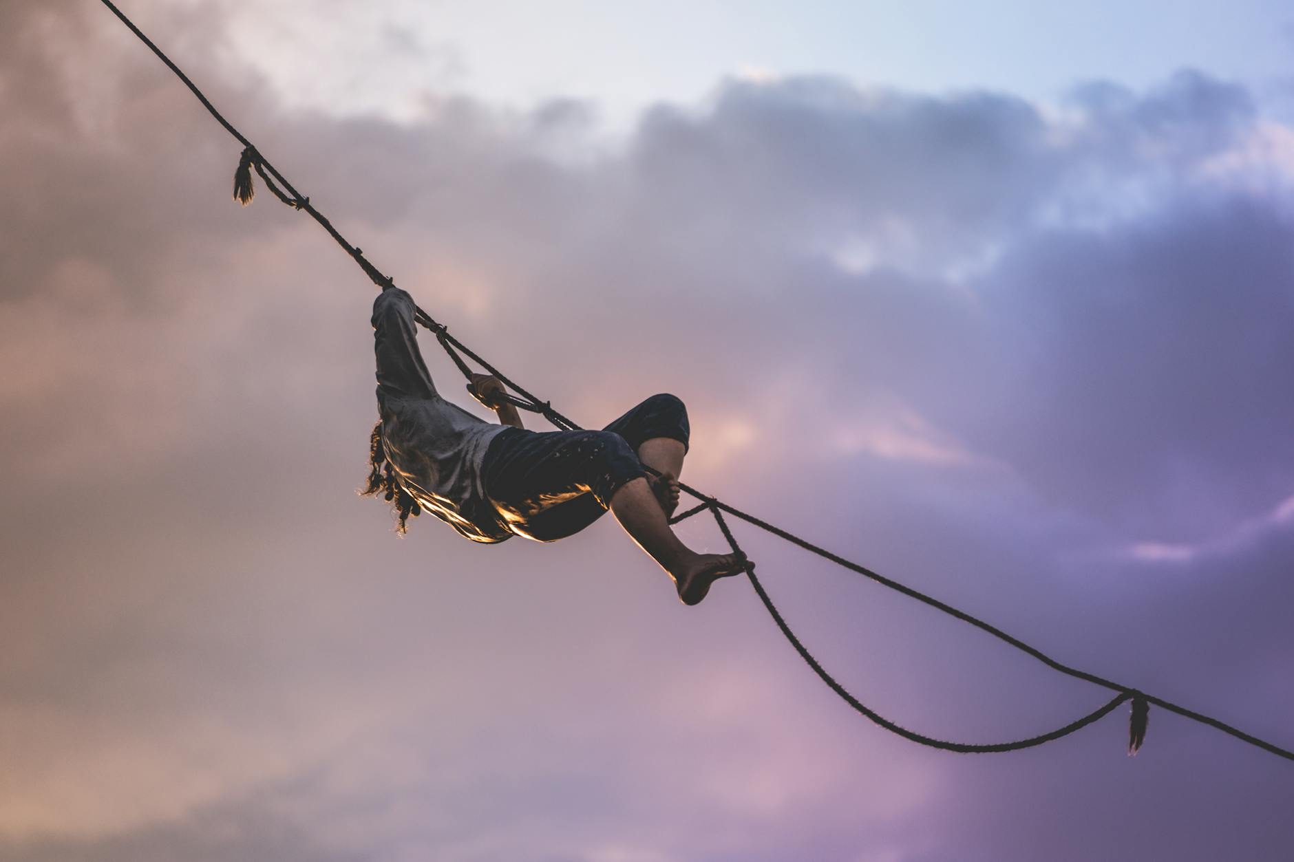 Unrecognizable male athlete climbing tightrope under cloudy sky