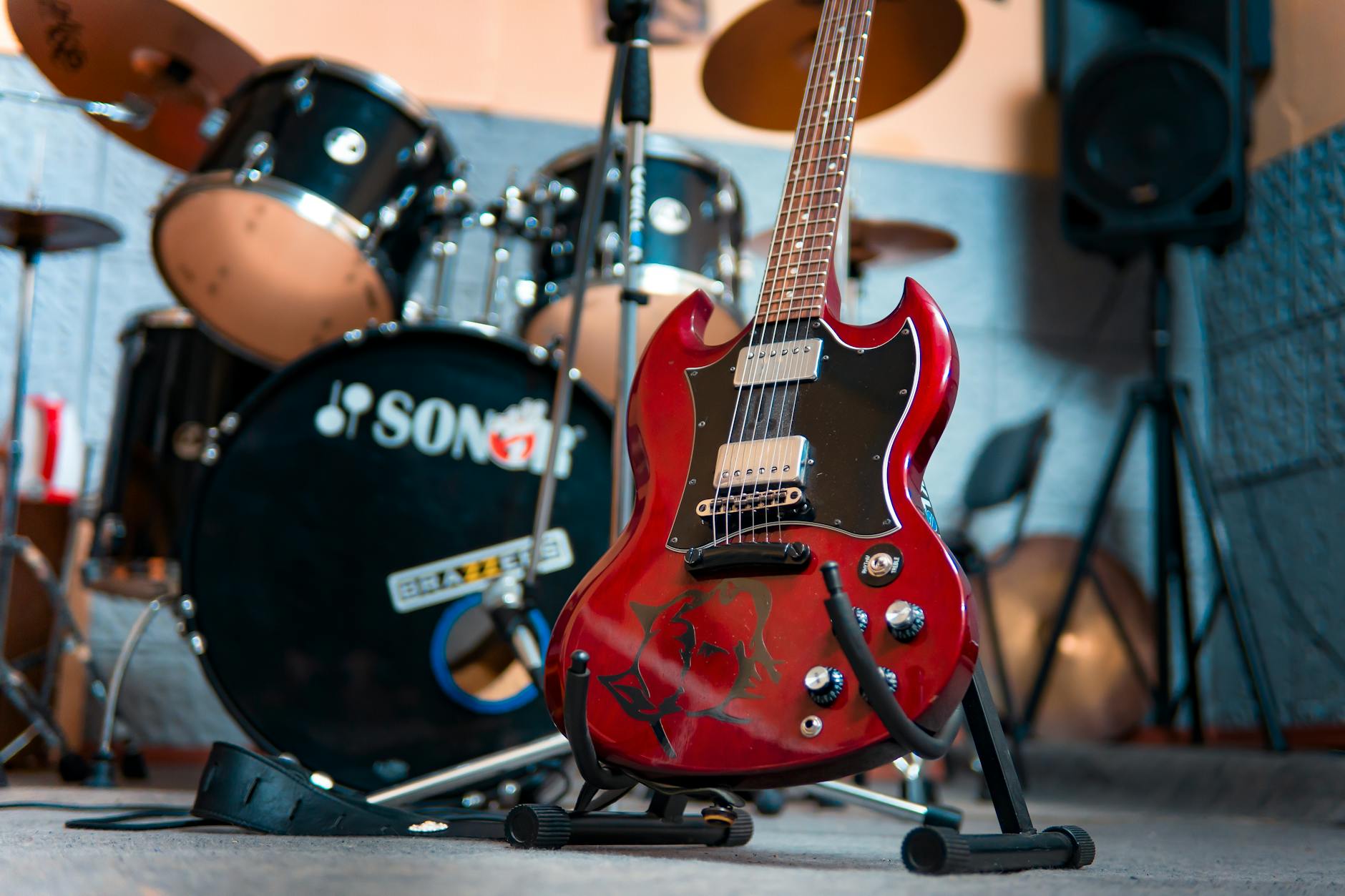 From below of modern electronic shiny guitar against drum kit and speakers in music studio