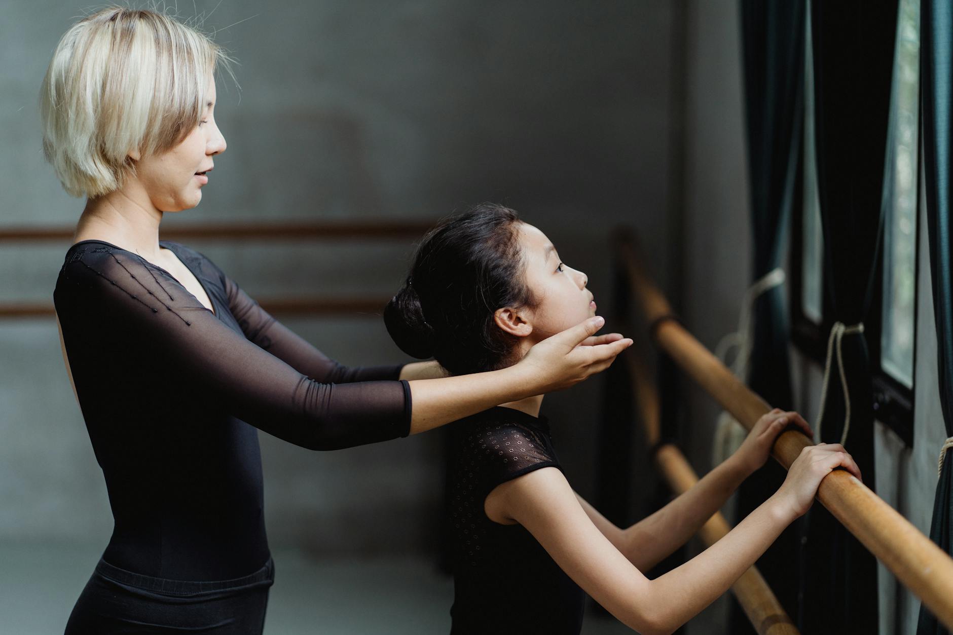 Side view of ballet instructor teaching concentrated girl near barre in modern studio