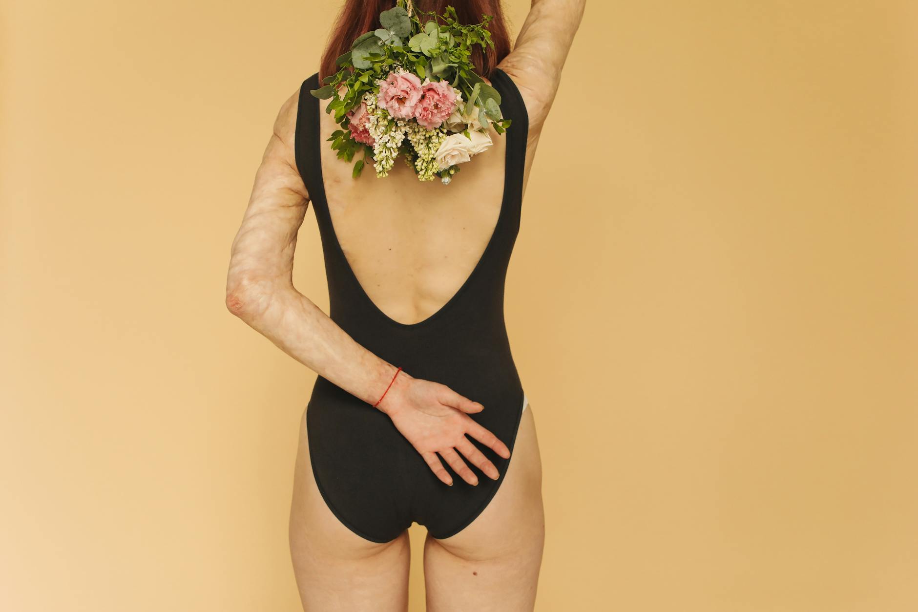 A Back View of a Woman in Black Bodysuit Holding Flowers