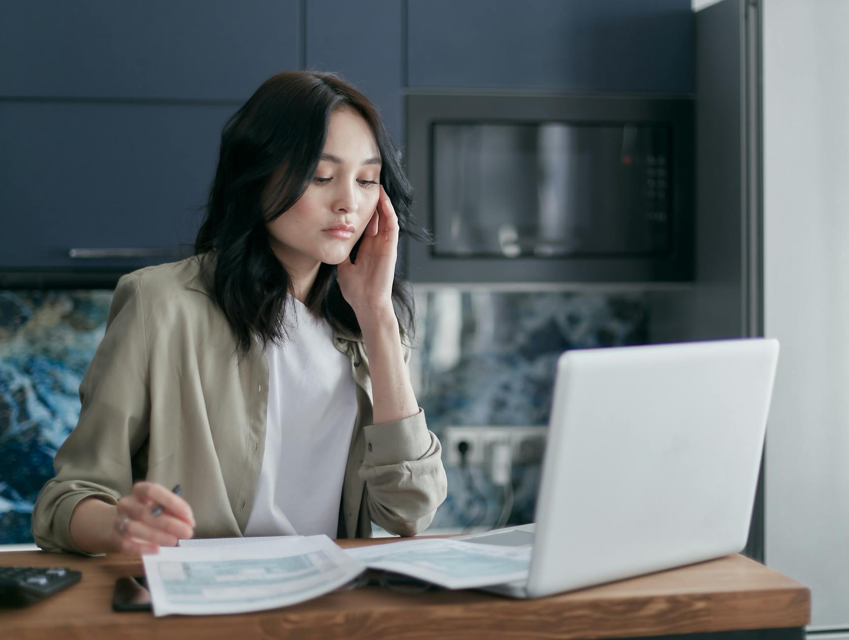 A Woman Sitting at a Table Looking at a Paper on a Laptop