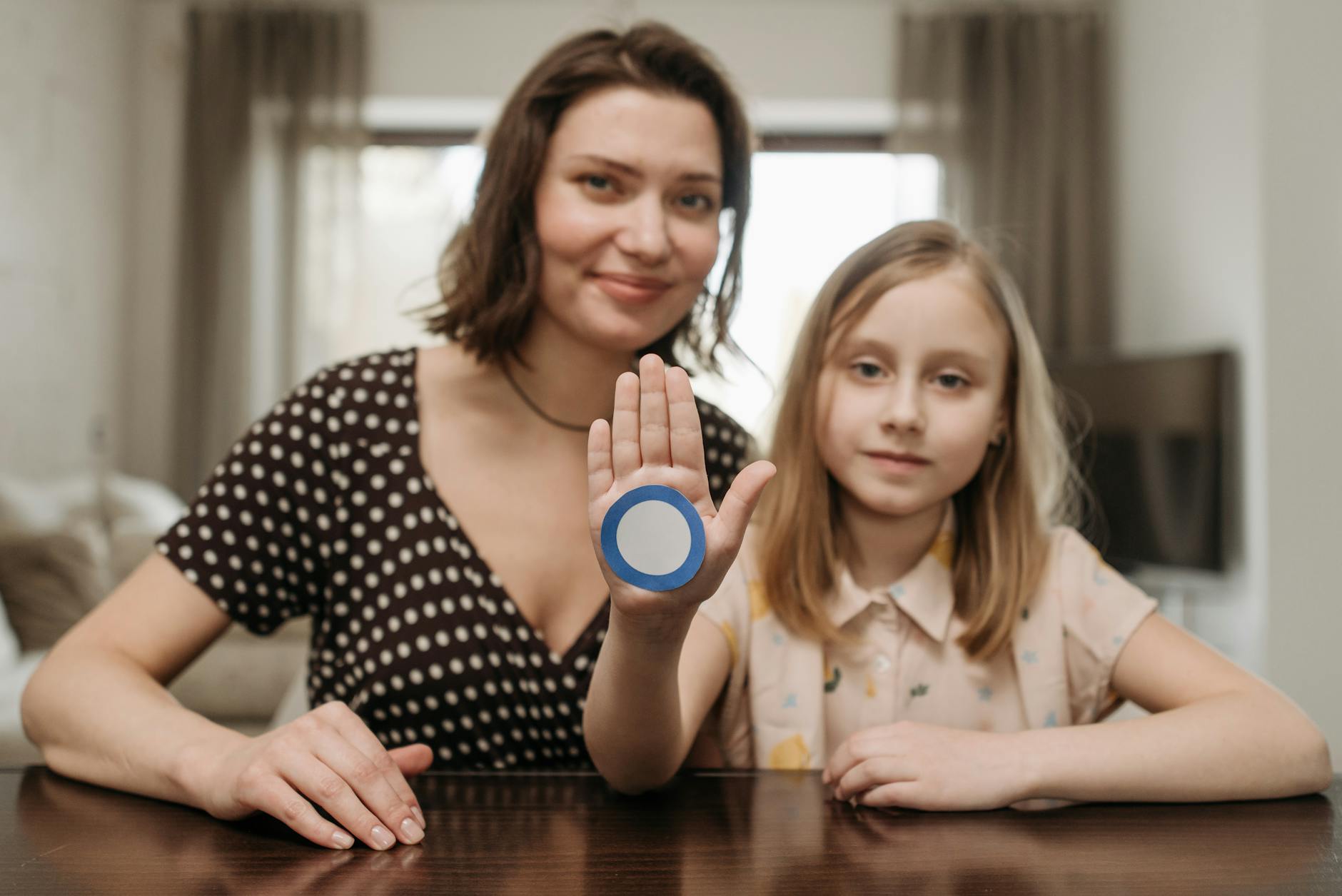 Woman and Girl Sitting at the Table and Girl Showing Her Hand with a Blue Diabetes Sign