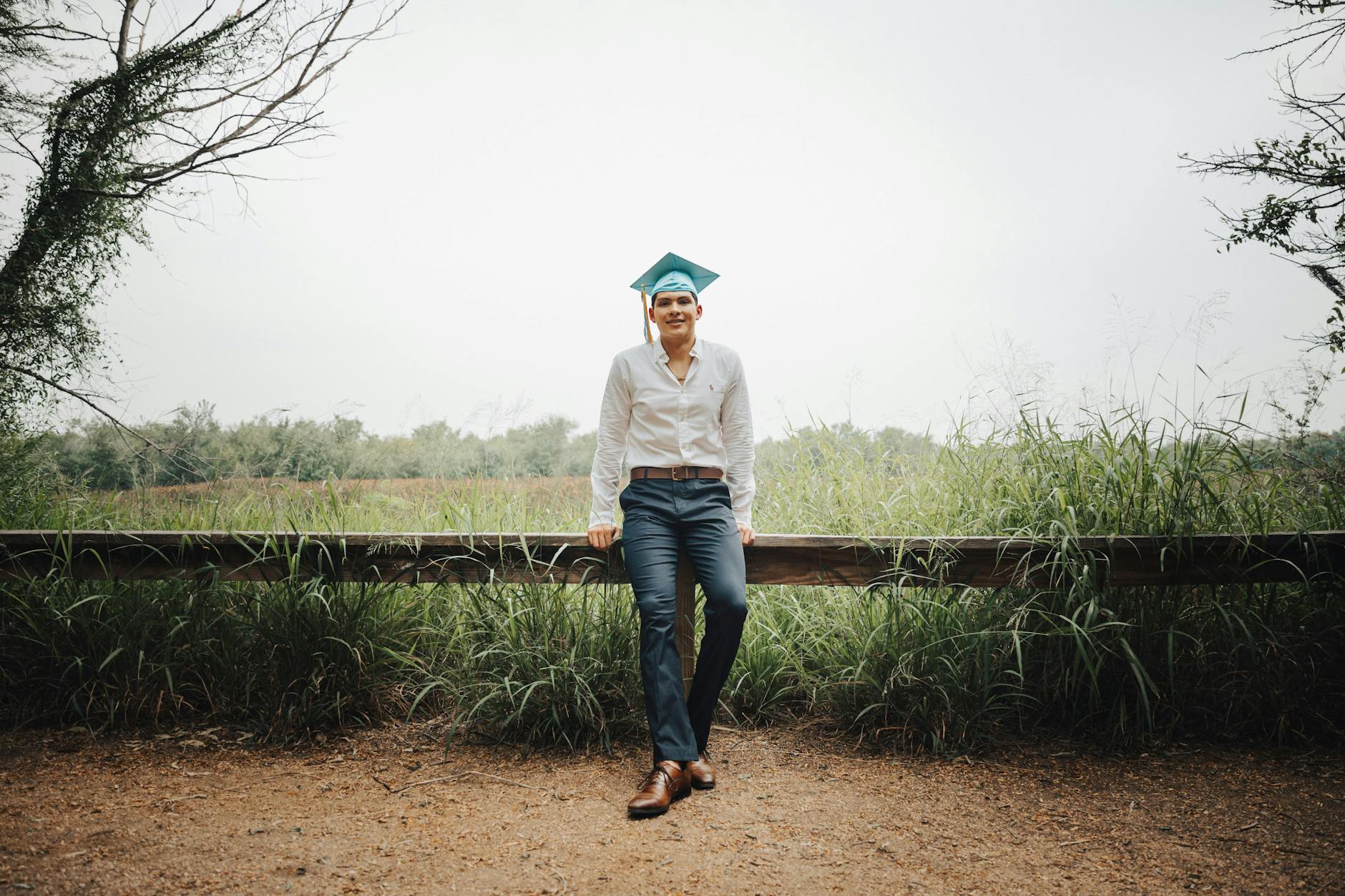 Man in Shirt and Academic Hat Sitting on Fence in Countryside